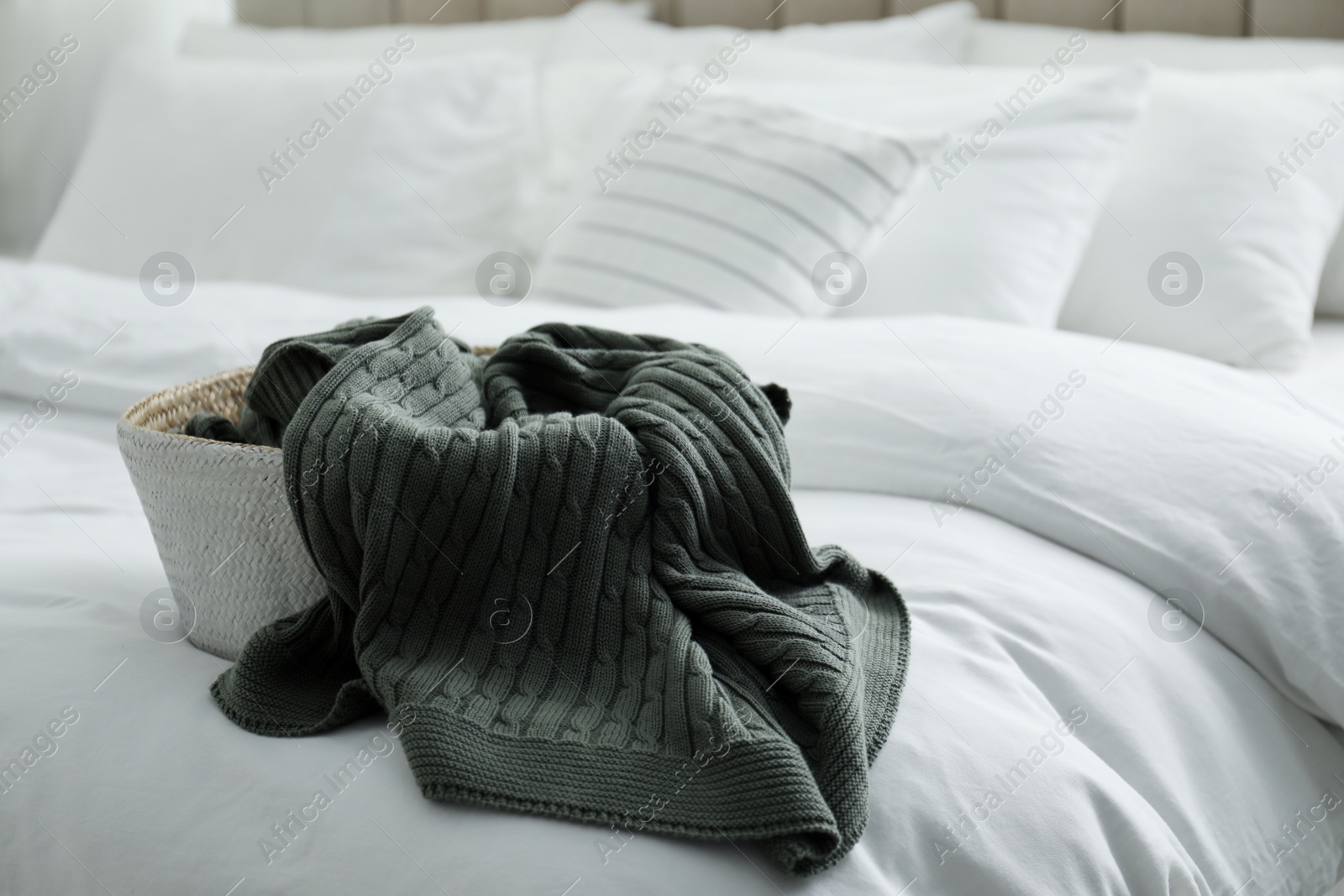 Photo of Basket with warm knitted plaid on bed indoors