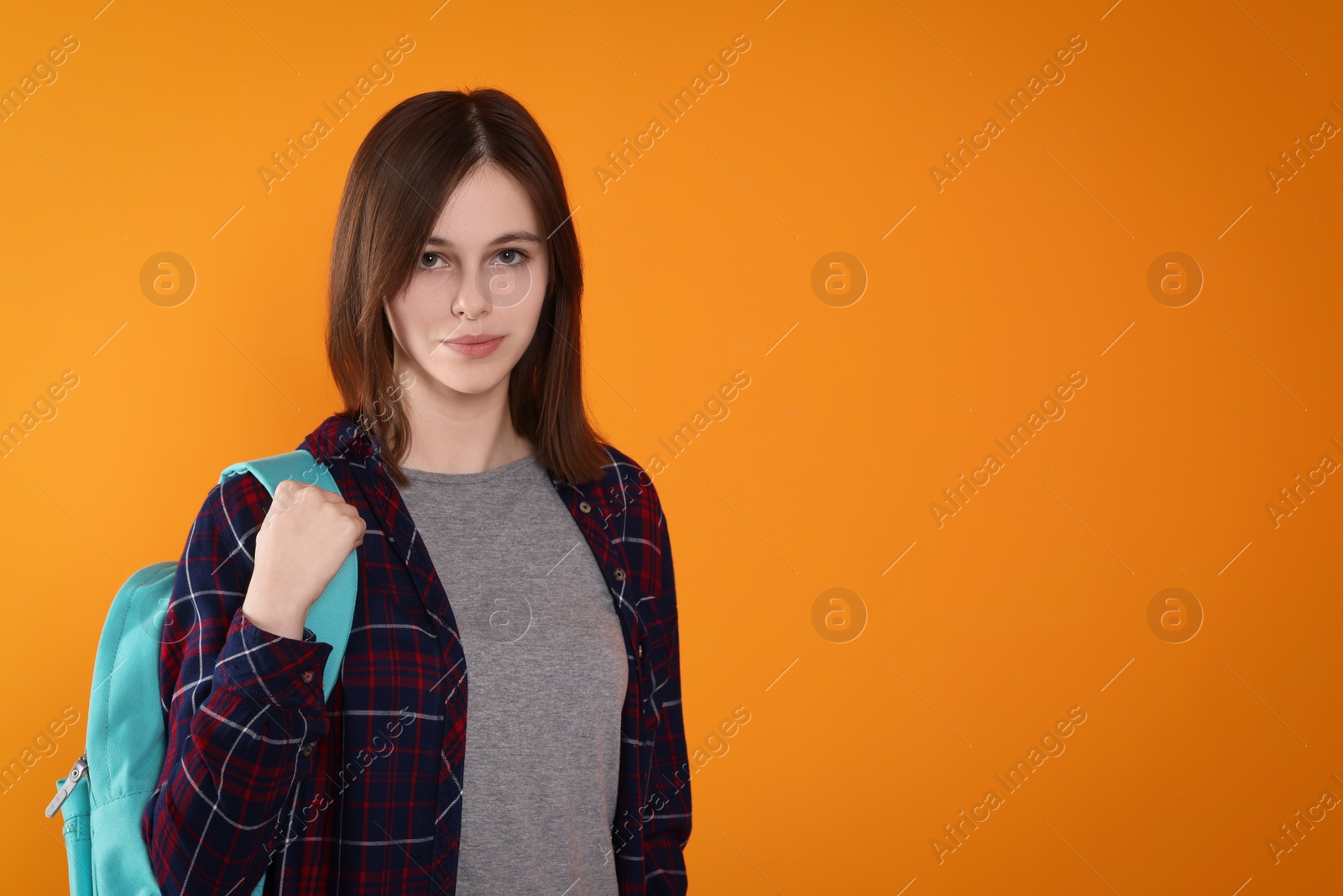 Photo of Portrait of cute teenage girl with backpack on orange background. Space for text