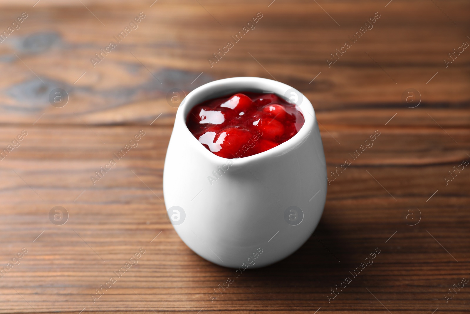 Photo of Fresh cranberry sauce in pitcher on wooden table, closeup