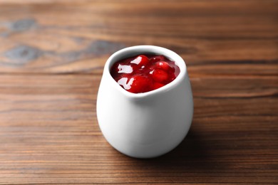 Photo of Fresh cranberry sauce in pitcher on wooden table, closeup