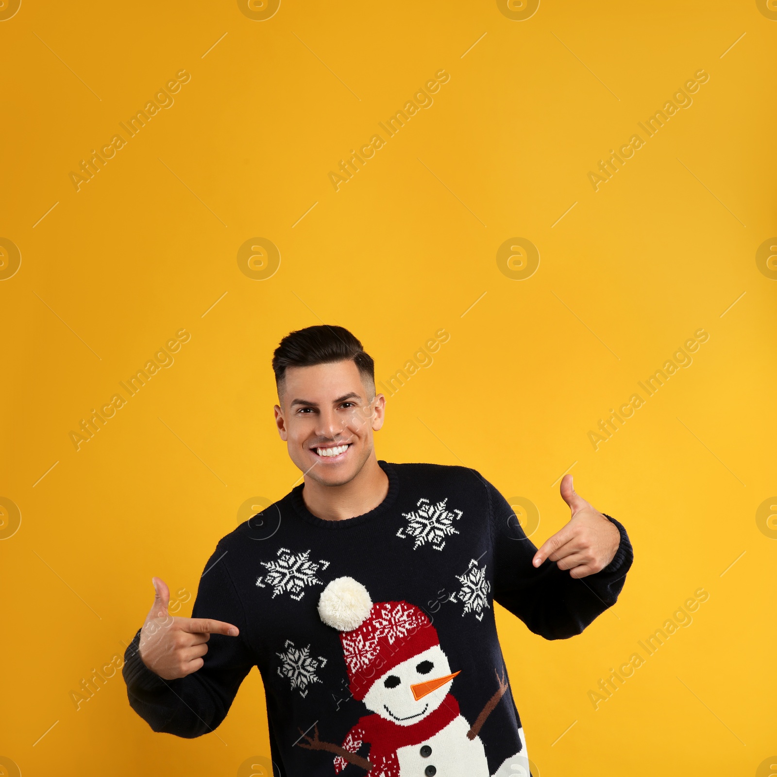 Photo of Happy man pointing on his Christmas sweater against yellow background