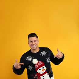 Happy man pointing on his Christmas sweater against yellow background