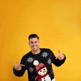 Photo of Happy man pointing on his Christmas sweater against yellow background