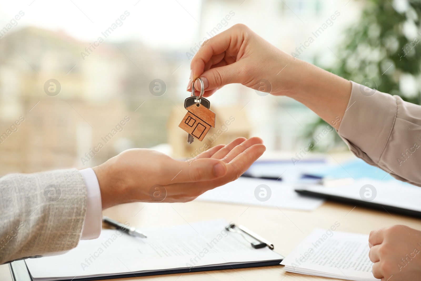 Photo of Real estate agent giving key with trinket to client in office, closeup