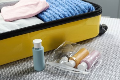 Photo of Plastic bag of cosmetic travel kit and suitcase on bed