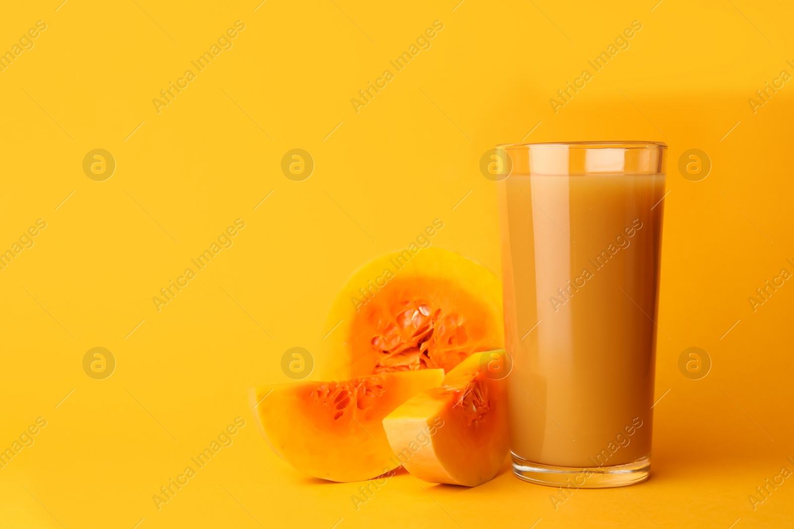 Photo of Glass with tasty pumpkin juice and cut pumpkin on orange background. Space for text