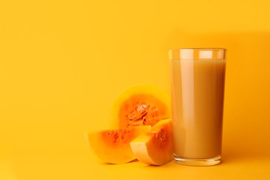 Photo of Glass with tasty pumpkin juice and cut pumpkin on orange background. Space for text