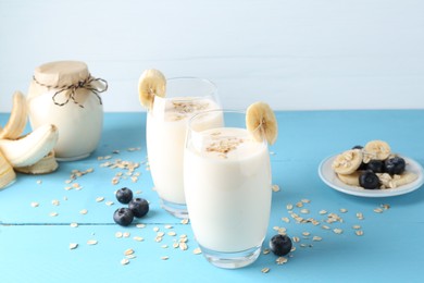 Photo of Tasty yogurt in glasses, oats, banana and blueberries on light blue wooden table