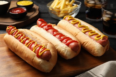 Photo of Delicious hot dogs with mustard and ketchup on black wooden table, closeup