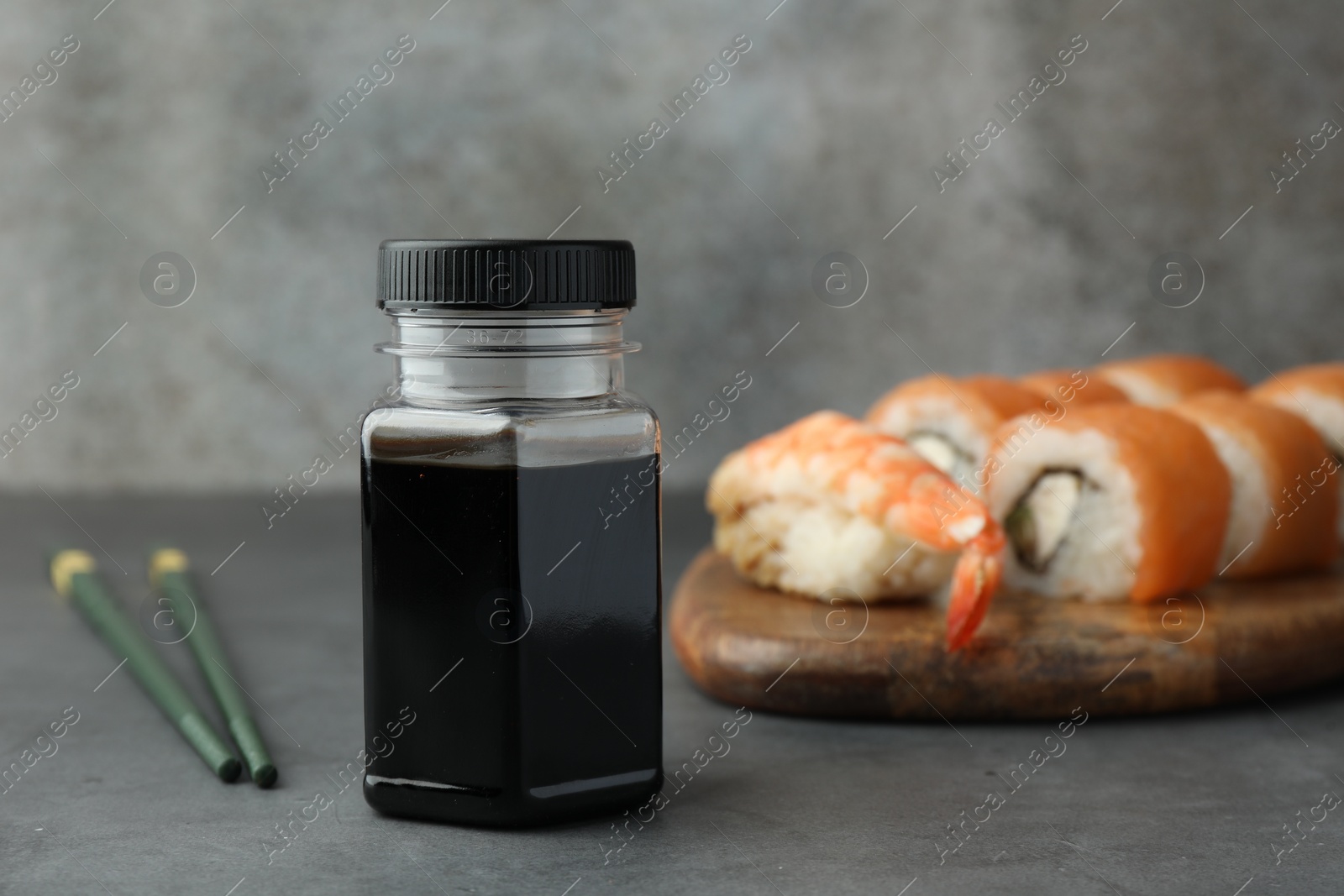 Photo of Bottle of tasty soy sauce, chopsticks and different types of sushi on grey table