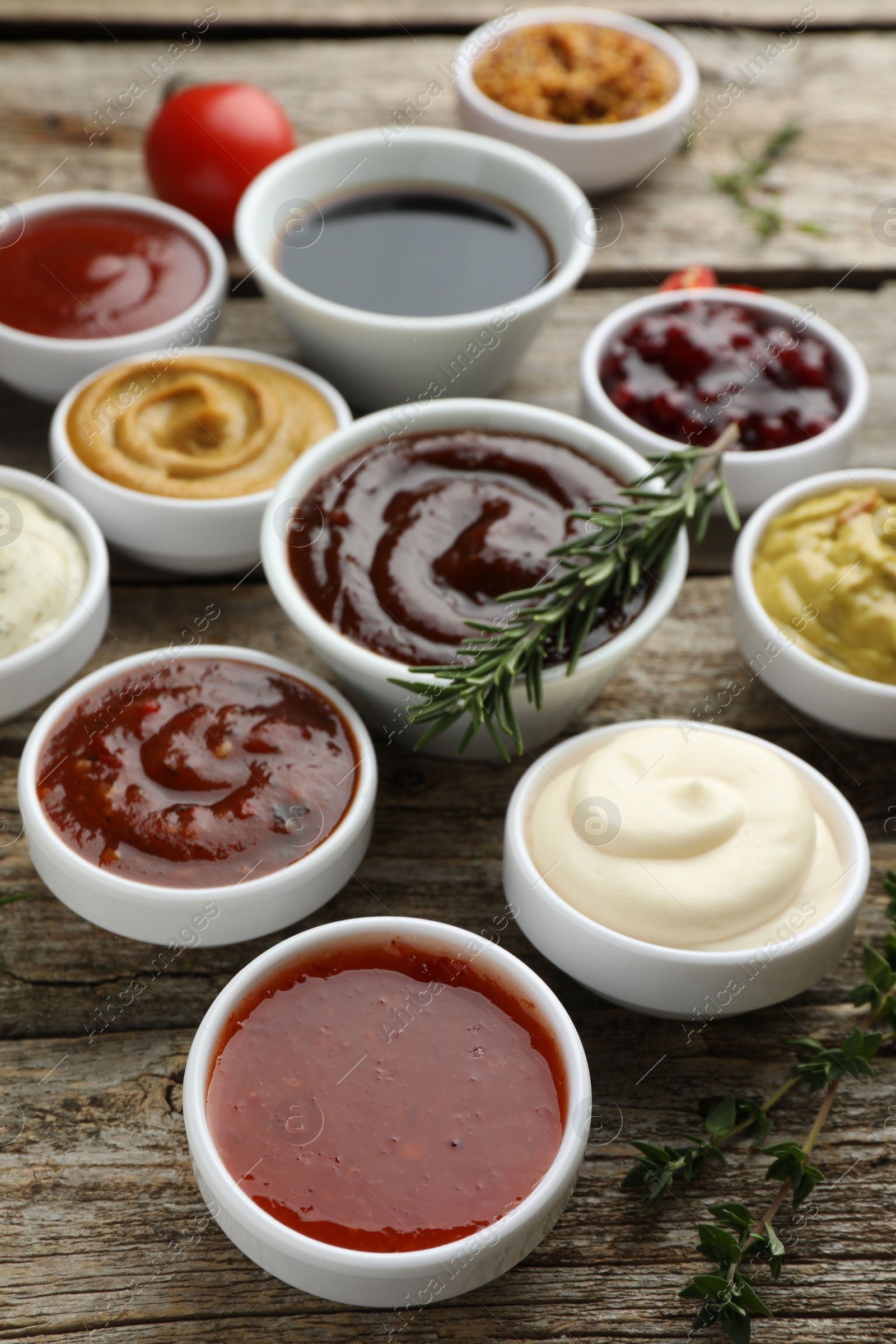 Photo of Different tasty sauces in bowls, rosemary and thyme on wooden table