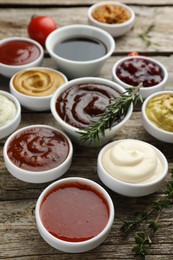 Photo of Different tasty sauces in bowls, rosemary and thyme on wooden table