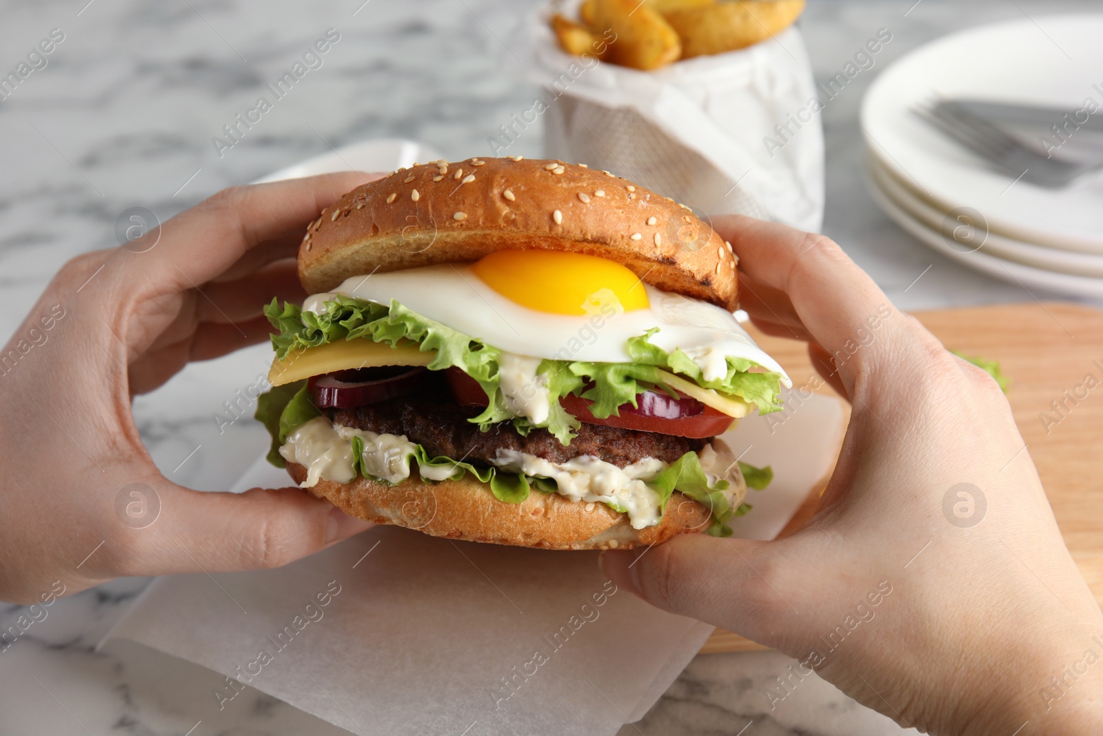 Photo of Woman holding tasty burger with fried egg over table, closeup