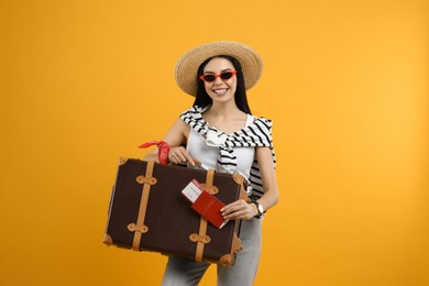 Photo of Happy female tourist with passport, ticket and suitcase on yellow background