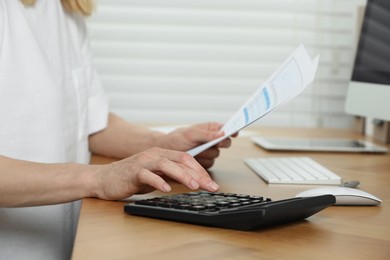 Photo of Professional accountant using calculator at wooden desk in office, closeup