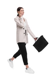 Photo of Beautiful businesswoman in suit with briefcase talking on smartphone walking against white background