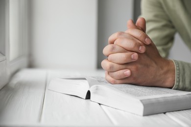 Photo of Religion. Christian man praying over Bible at white wooden the table, closeup. Space for text