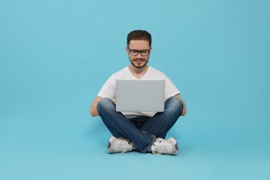 Smiling man sitting and using laptop on light blue background