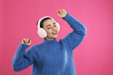 Photo of Beautiful young woman wearing earmuffs on pink background