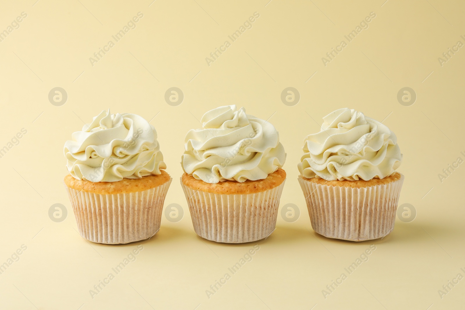 Photo of Tasty vanilla cupcakes with cream on pale yellow background