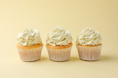 Photo of Tasty vanilla cupcakes with cream on pale yellow background