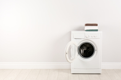 Photo of Modern washing machine with stack of towels near white wall, space for text. Laundry day