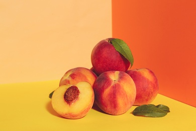 Photo of Fresh ripe peaches and green leaves on color background