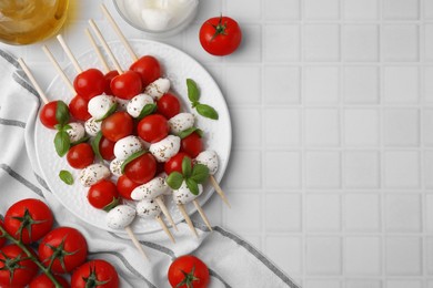 Photo of Caprese skewers with tomatoes, mozzarella balls, basil and spices on white tiled table, flat lay. Space for text