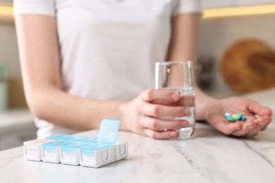 Woman with pills, organizer and glass of water at white marble table, closeup