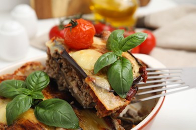 Photo of Spatula with piece of delicious eggplant lasagna over baking dish at table, closeup