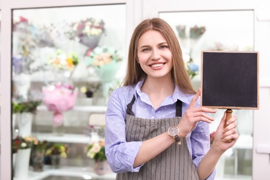 Photo of Female florist holding small chalkboard at workplace
