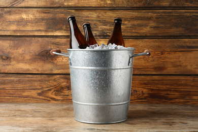 Photo of Metal bucket with beer and ice cubes on wooden background