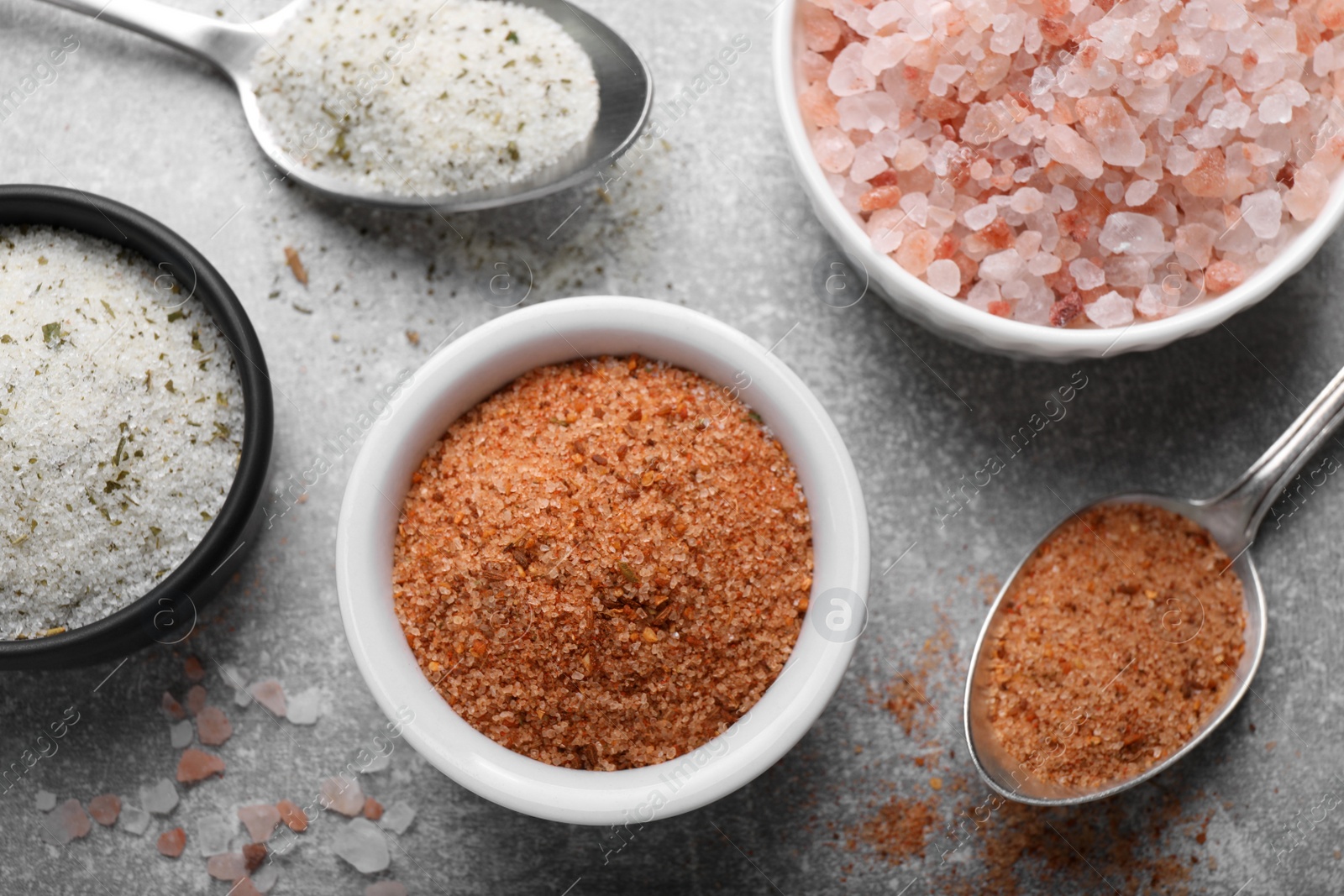 Photo of Different kinds of salt on grey table, flat lay