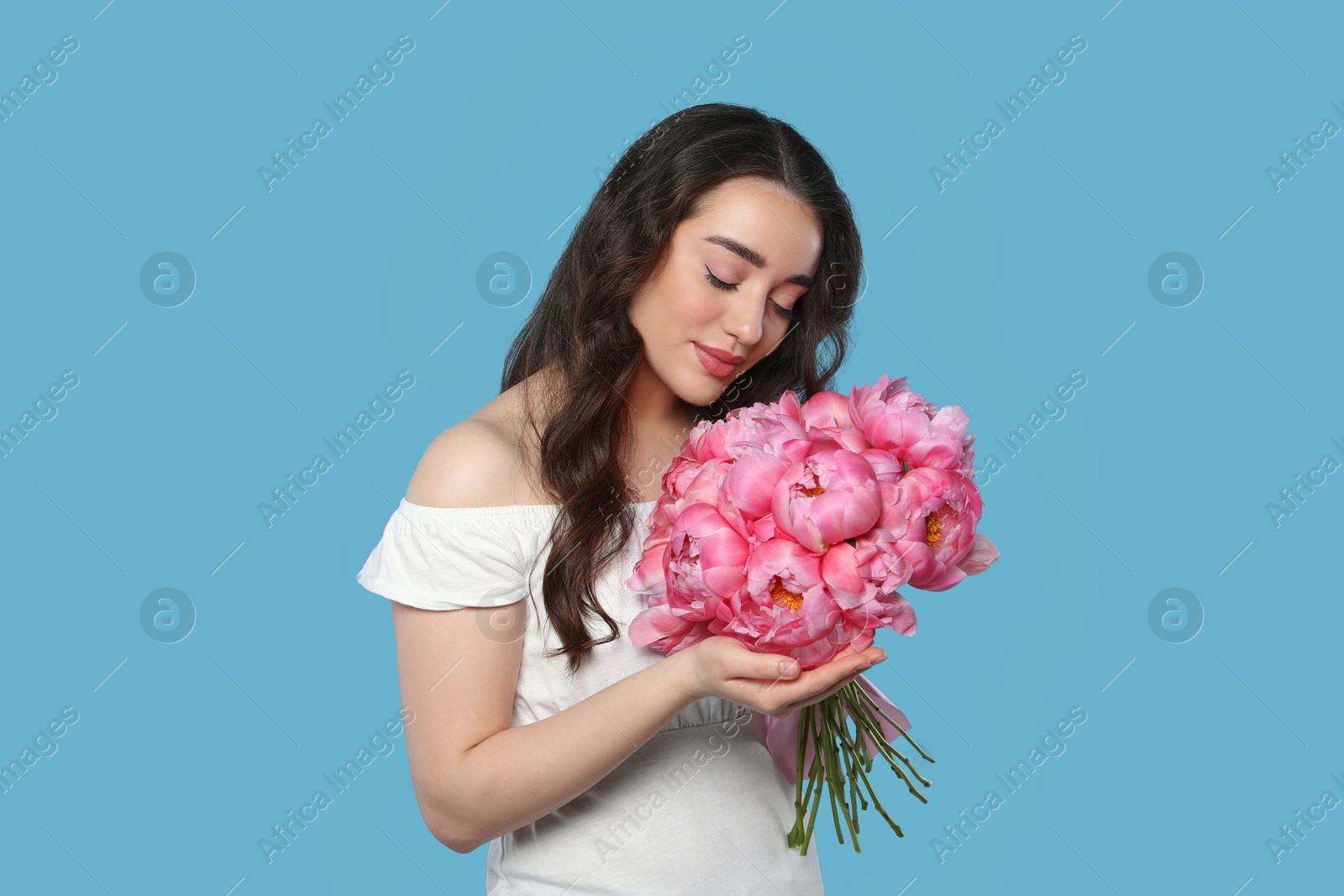 Photo of Beautiful young woman with bouquet of pink peonies on light blue background