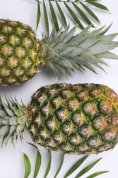 Photo of Whole ripe pineapples and green leaves on white background, flat lay