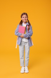Happy schoolgirl with books on orange background