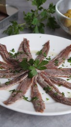 Plate with anchovy fillets and parsley on table, closeup