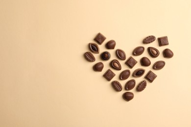 Photo of Heart made with delicious chocolate candies on beige background, top view. Space for text