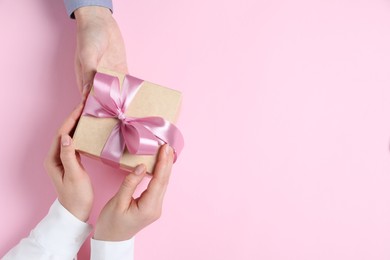 Photo of Man giving gift box to woman on pink background, top view. Space for text