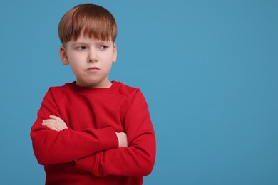 Portrait of sad little boy on light blue background, space for text