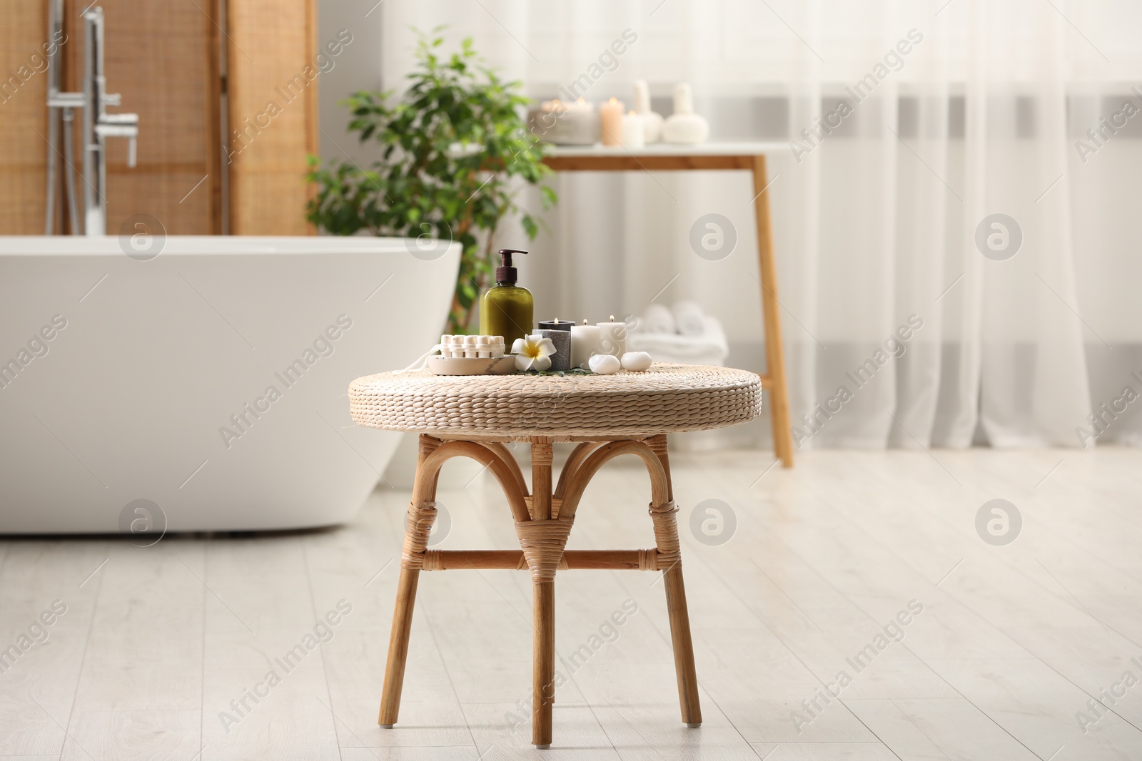 Photo of Spa products, burning candles and plumeria flower on small table in bathroom