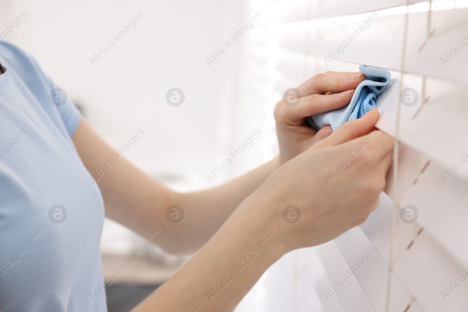 Photo of Woman with microfiber cloth wiping blinds at home, closeup