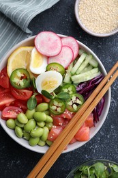 Photo of Poke bowl with salmon, edamame beans and vegetables on black table, flat lay