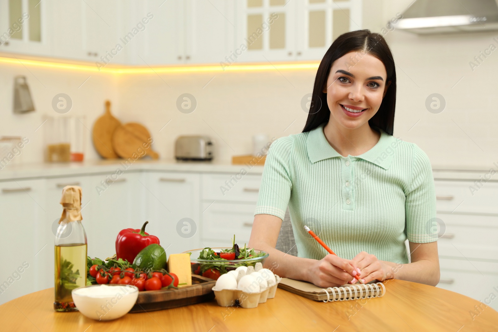 Photo of Happy woman writing in notebook near products at table. Keto diet