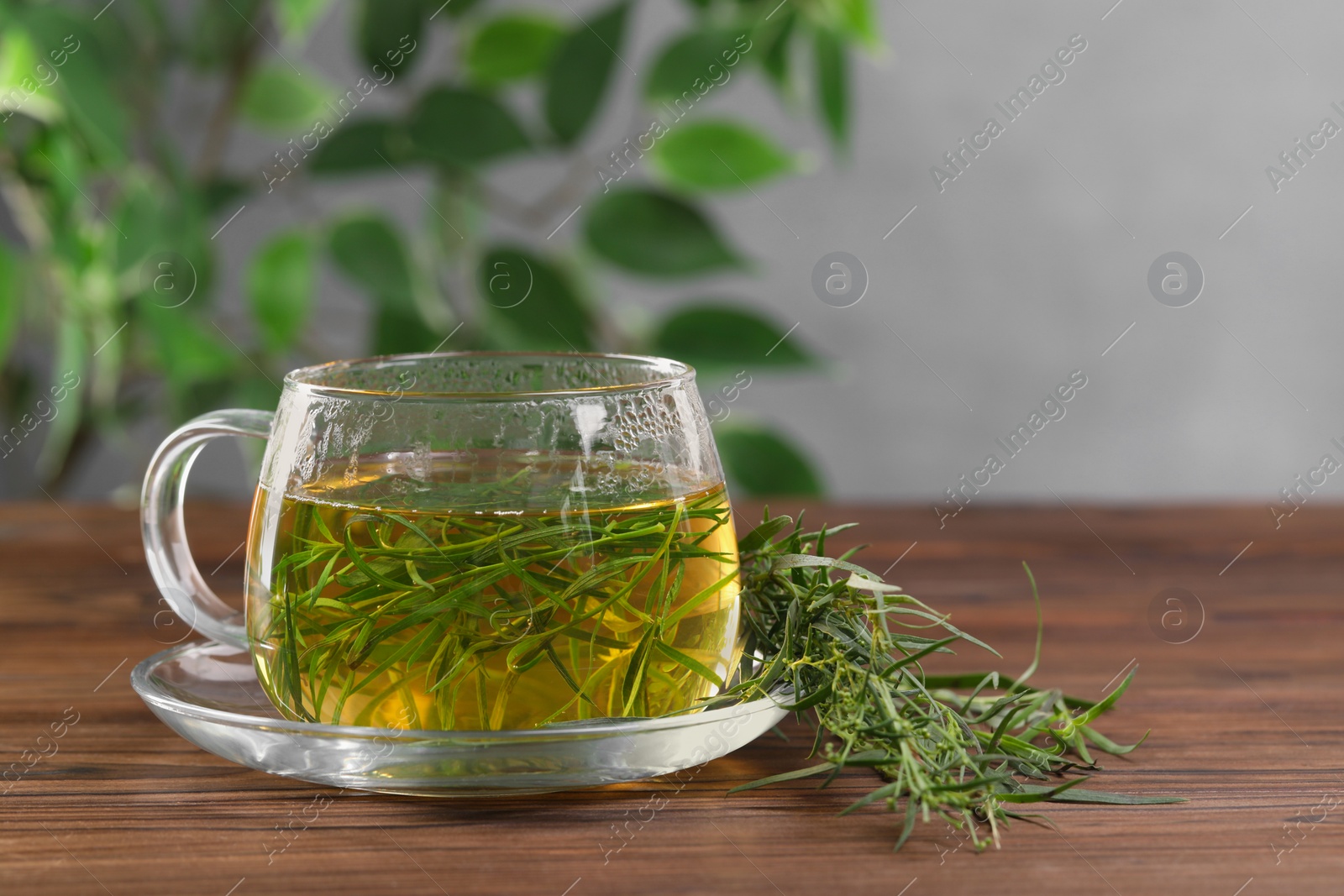 Photo of Cup of homemade herbal tea and fresh tarragon leaves on wooden table. Space for text