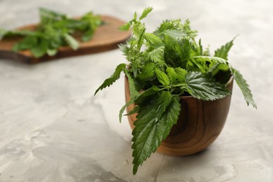 Fresh stinging nettle leaves in wooden bowl on light grey table, closeup. Space for text