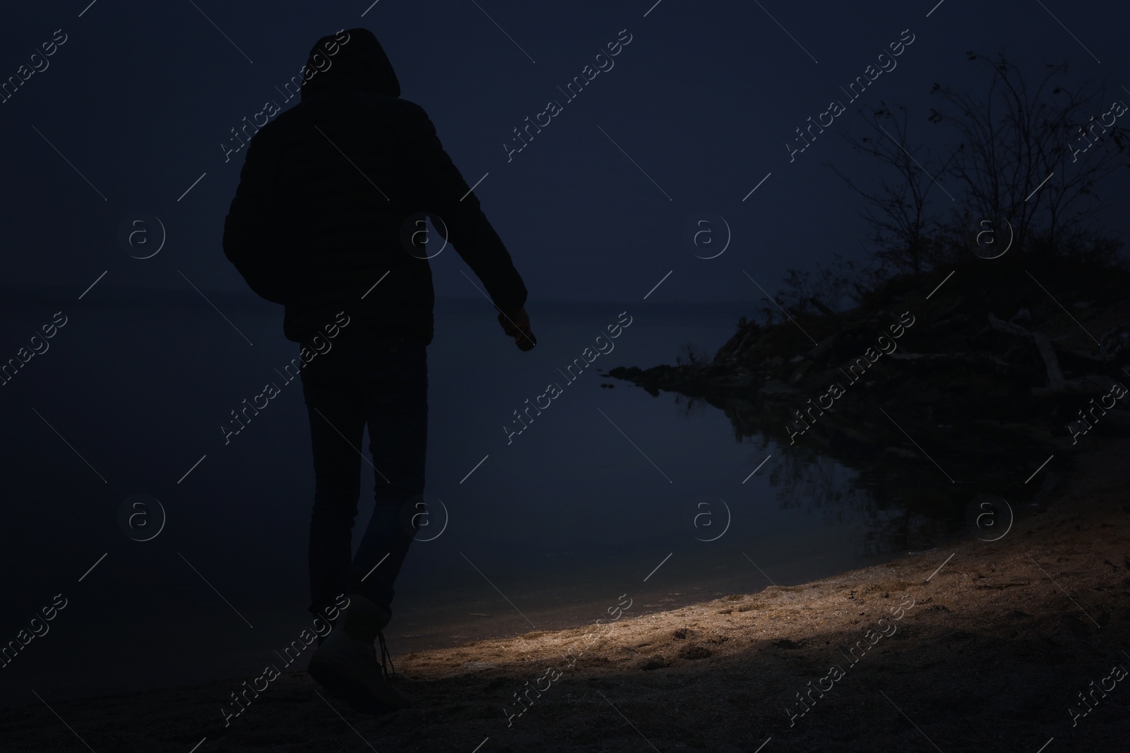 Photo of Man with flashlight walking near river in evening