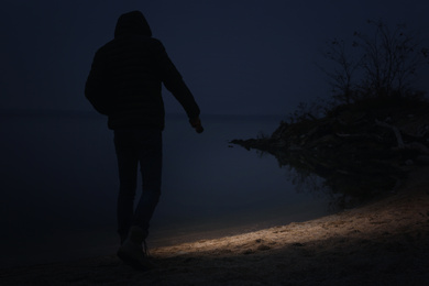 Photo of Man with flashlight walking near river in evening