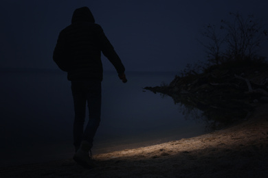 Man with flashlight walking near river in evening