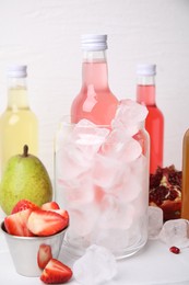 Tasty kombucha in bottles, glass with ice and fresh fruits on white table